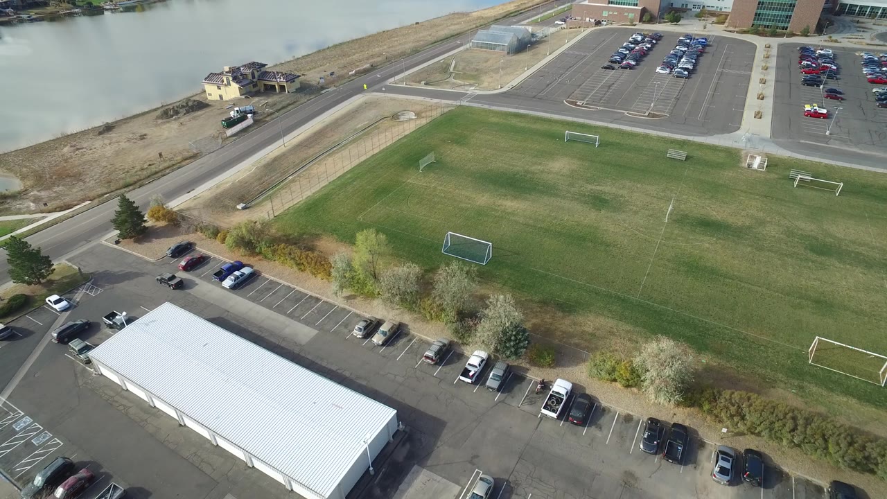 Aerial view in Hidden Lake, Colorado with the green field centered, small goals on the grass, parking lots at the top and bottom edges, and no visible people.
