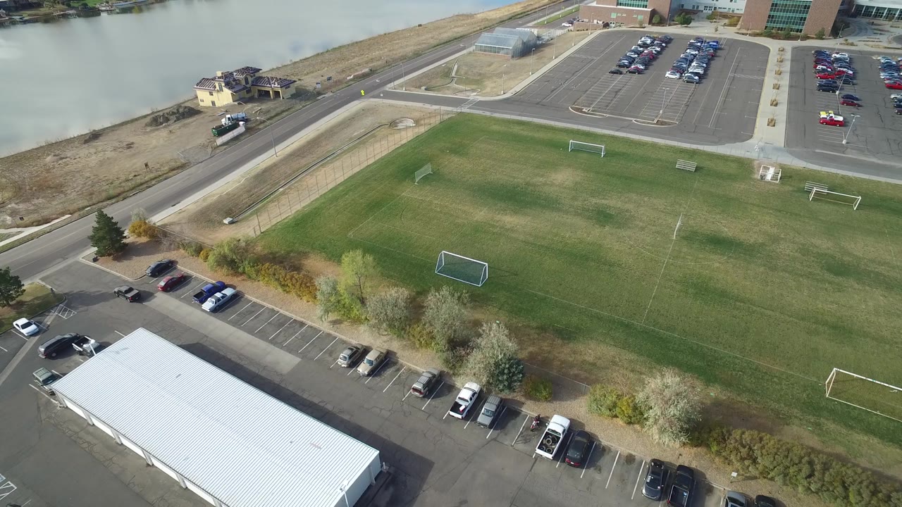 Drone view of a green field, road, cars, and nearby water.