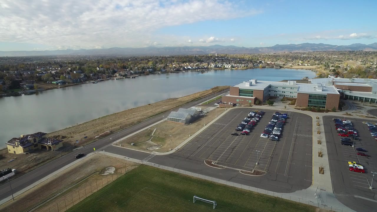 Aerial view of parking lots, a building, sports grass, and water beyond.