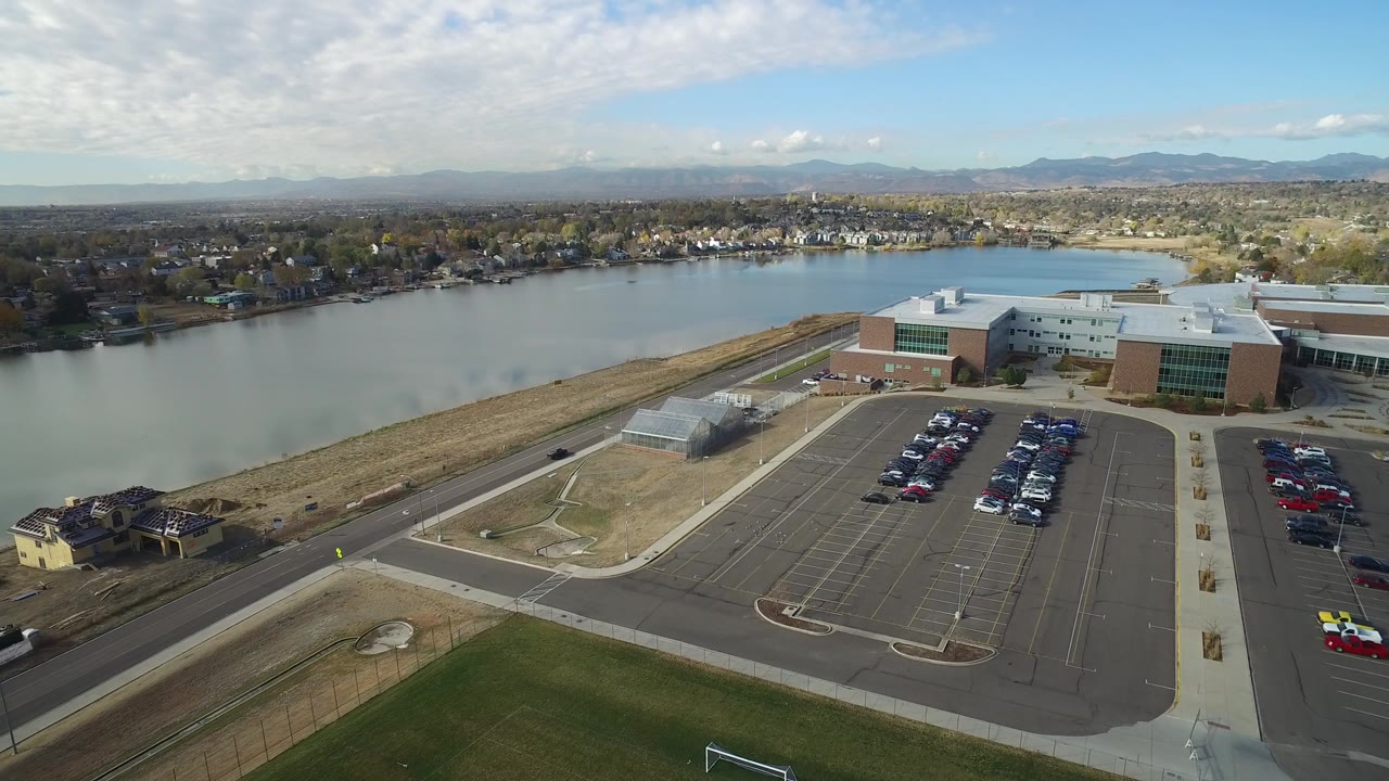 Aerial view of a parking lot, large building, lake, homes, and mountains.