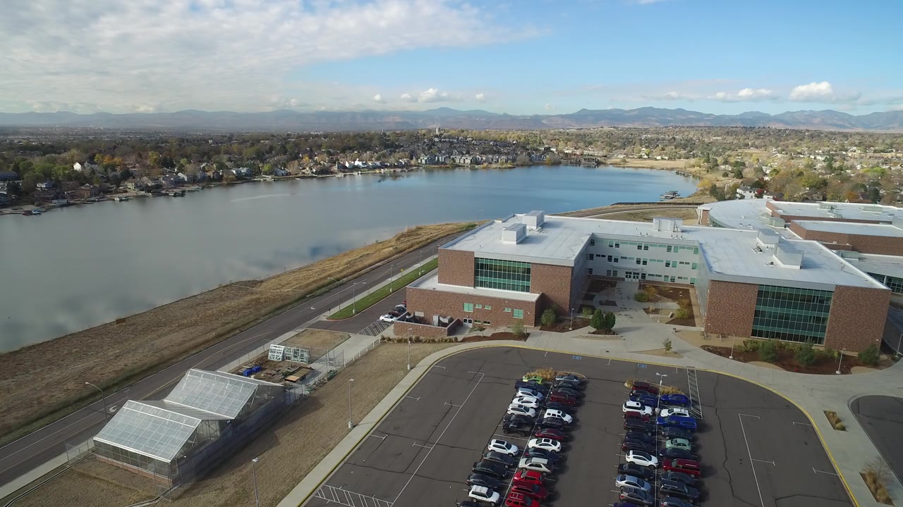 Aerial view of a brick building beside a lake and parking lot.