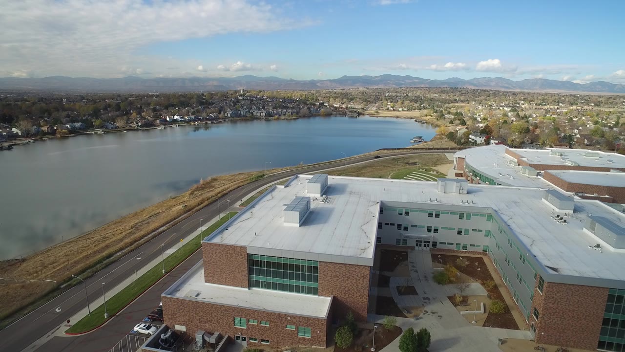 Aerial view of a lakeside building roof, road, lake, homes, and distant mountains.