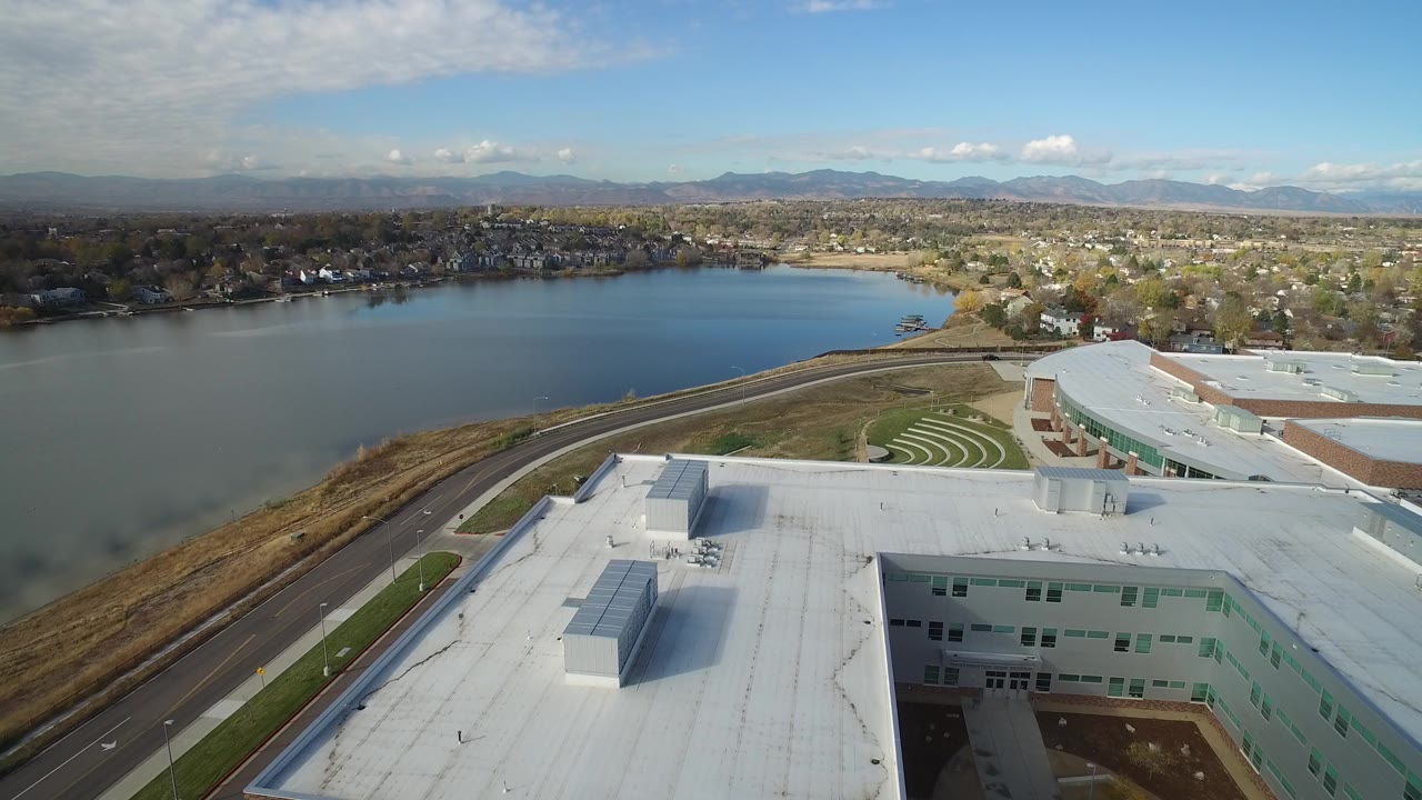 Aerial view over a white-roofed building toward a lake and suburban homes.