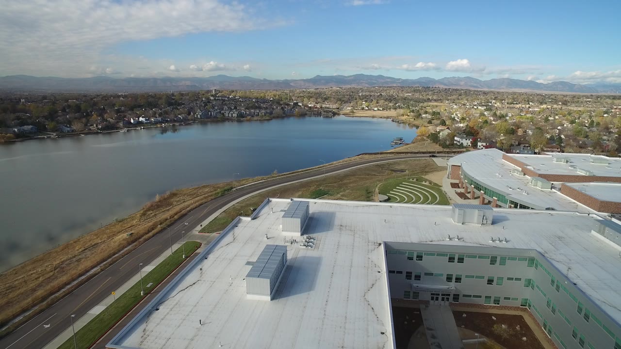 One second into the Hidden Lake, Colorado clip, the roofline and rooftop units stay prominent while the lake, road, neighborhood, and mountain horizon remain visible with no visible people.