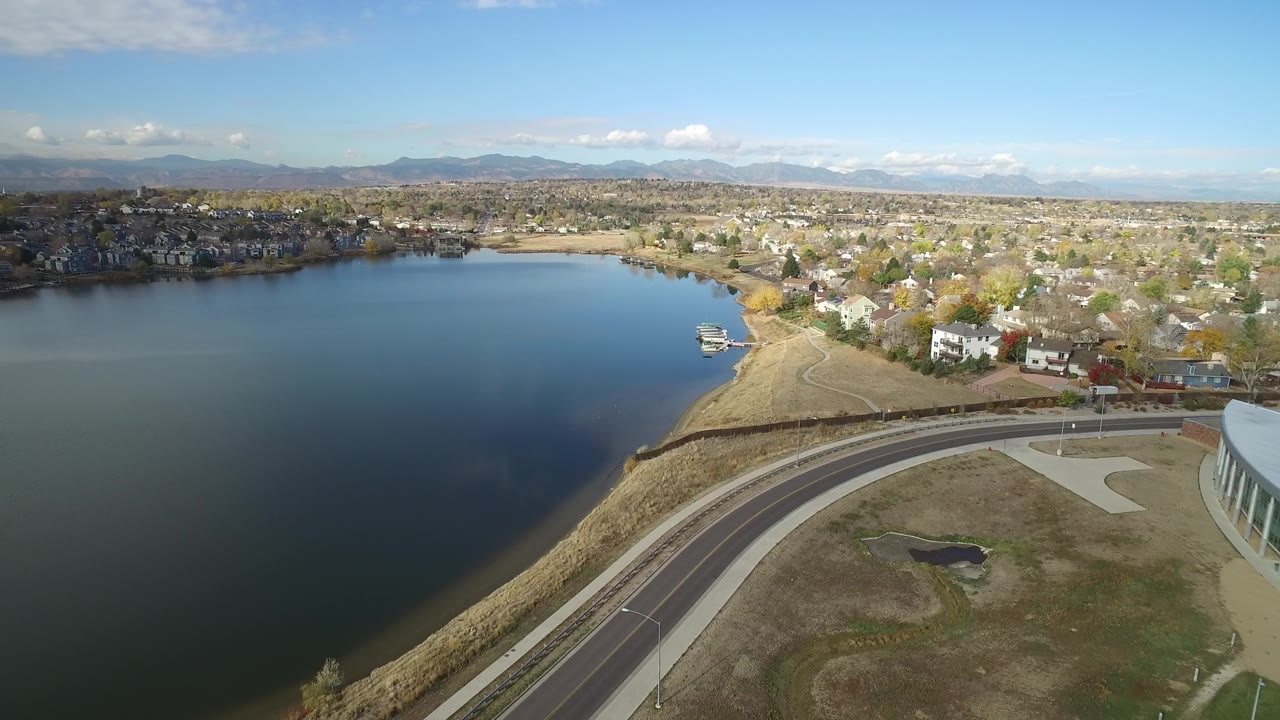 Aerial view of a lake beside a curved road and suburban homes.