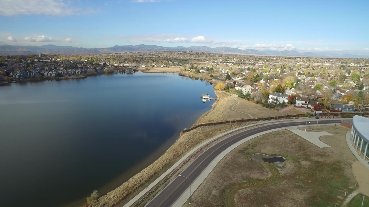 A second aerial view of Hidden Lake, Colorado, keeps the lake on the left, the curved road in the lower frame, homes along the shore, and no visible people.