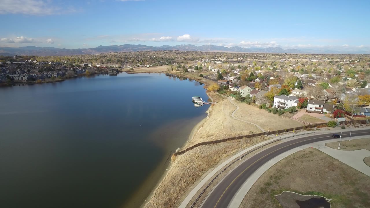 Aerial view of a lake, sandy shoreline, curved road, and residential neighborhood