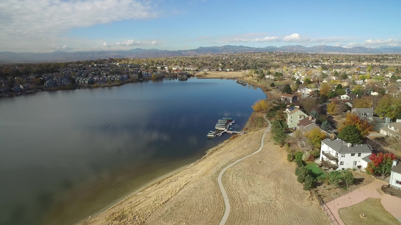 Aerial view of a lake beside suburban homes and a shoreline path.