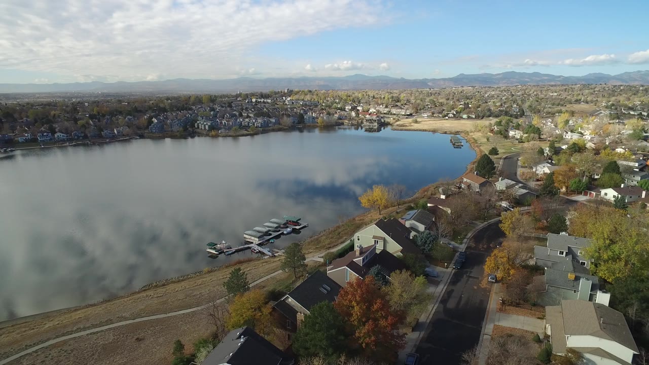 Aerial view in Hidden Lake, Colorado, showing a glassy lake surface, clustered shoreline homes, docks near the lower left, and no visible people.