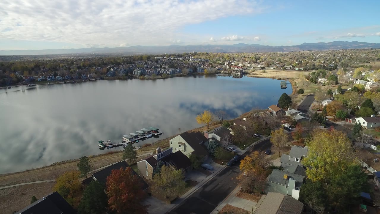 Aerial view over Hidden Lake, Colorado with lakeside homes in the foreground, docks along the shore, cloud reflections on the water, and no visible people.