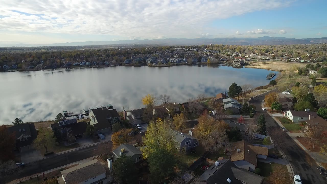 Aerial view of homes beside a calm lake with distant hills.