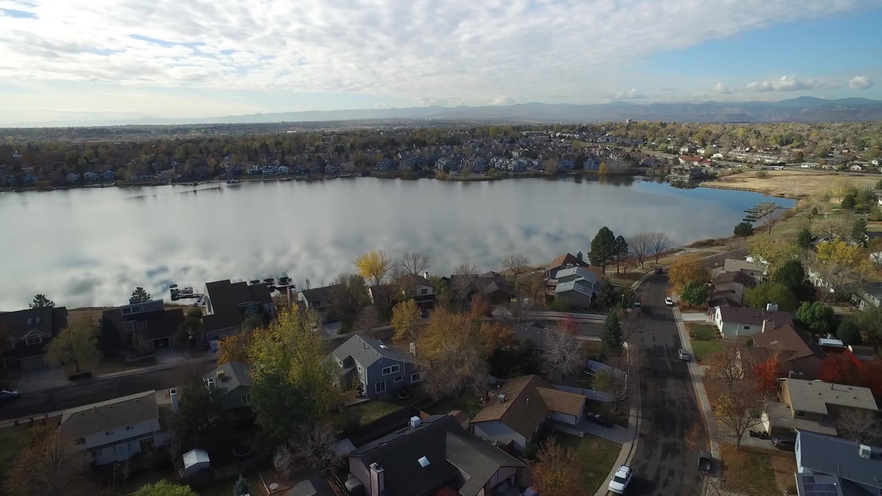 Aerial view over Hidden Lake, Colorado, showing foreground streets and homes below a reflective lake surface, with the opposite shoreline and no visible people.