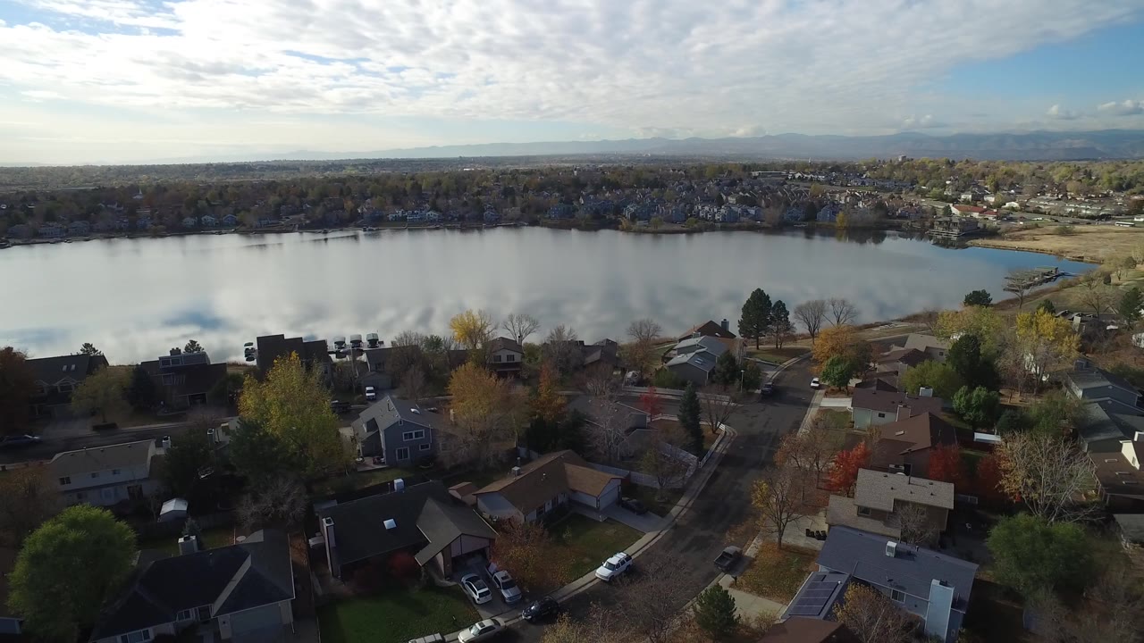 Aerial view over Hidden Lake, Colorado with residential rooftops in the foreground, a broad lake in the midground, distant horizon, and no visible people.