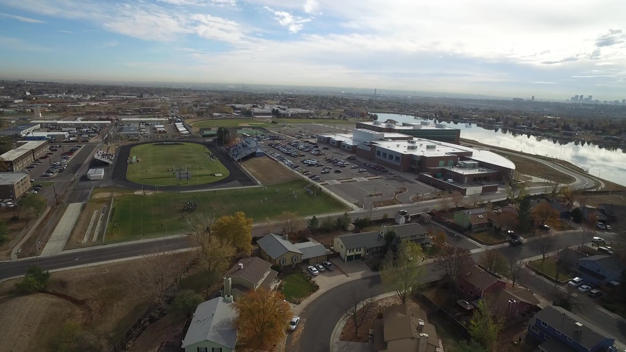 Aerial view of a green field, neighborhood streets, homes, a large building, and a lake.