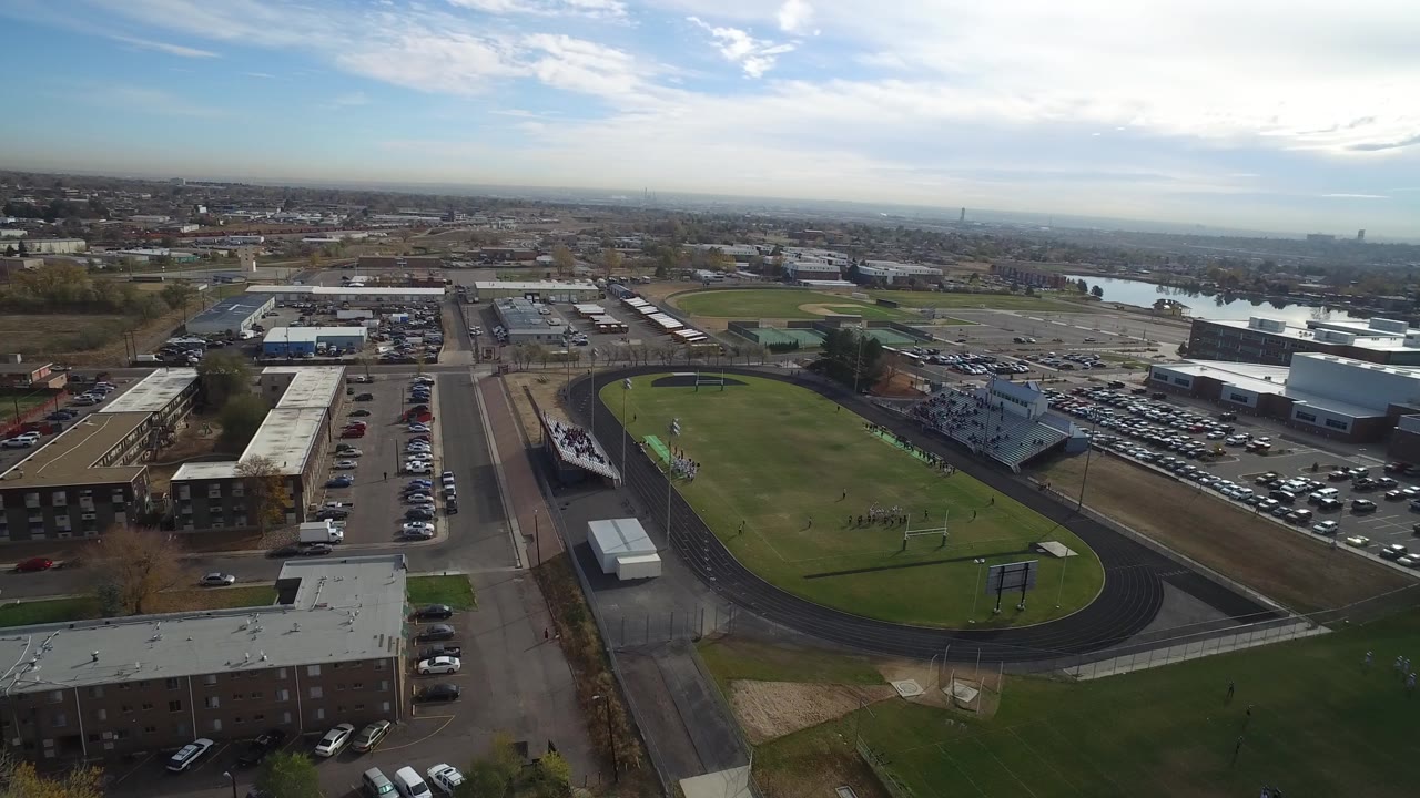 Aerial view of a football field and running track beside low buildings and parking lots.