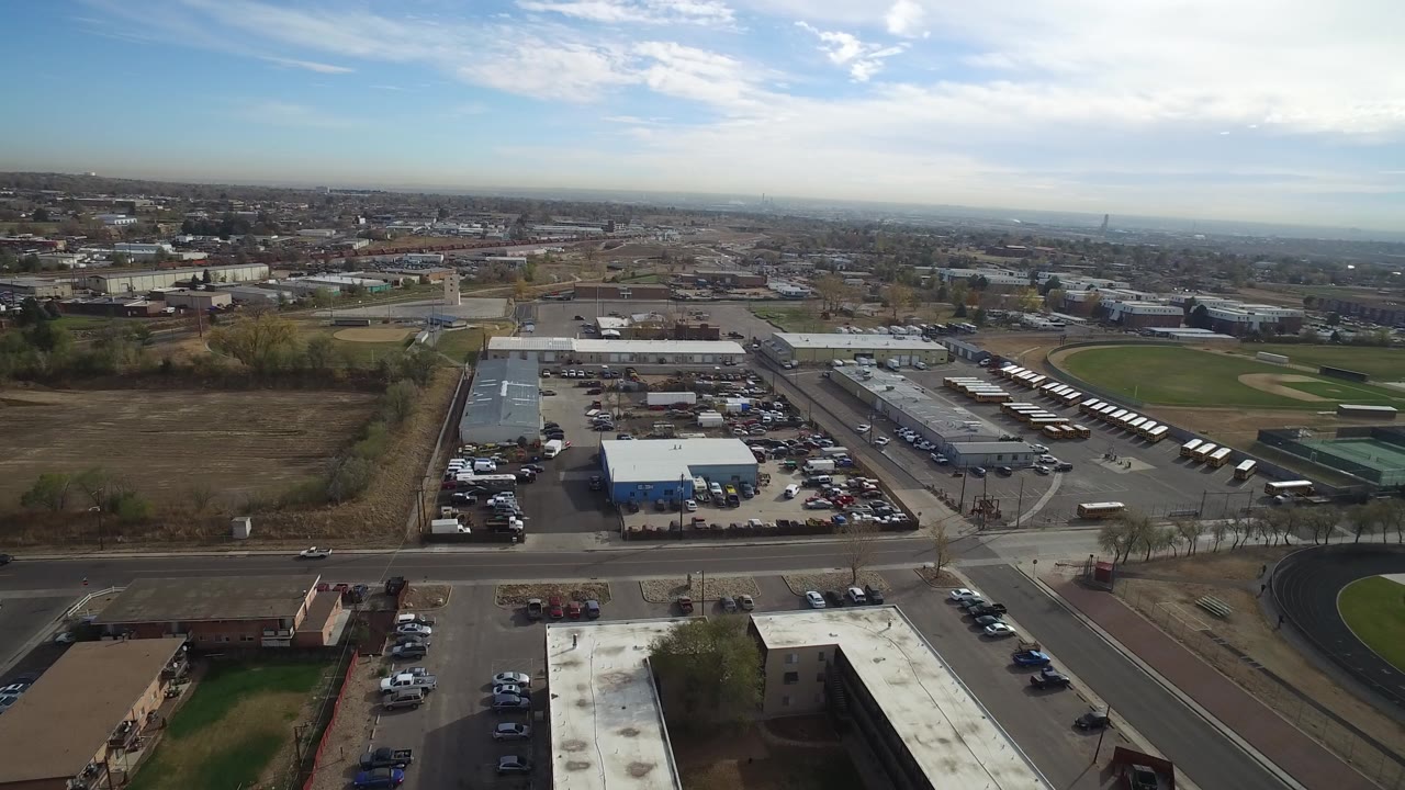 Aerial view of roads, parking lots, industrial buildings, fields, and distant suburbs.