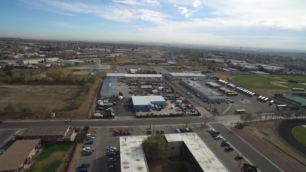 Aerial view in Hidden Lake, Colorado centered on a blue-and-white warehouse, surrounding parked cars, nearby roads, open brown fields, and no visible people.