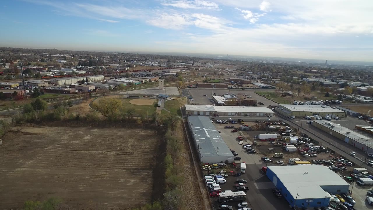 Drone-style view of warehouses, a parking lot, roads, and a wide city horizon.