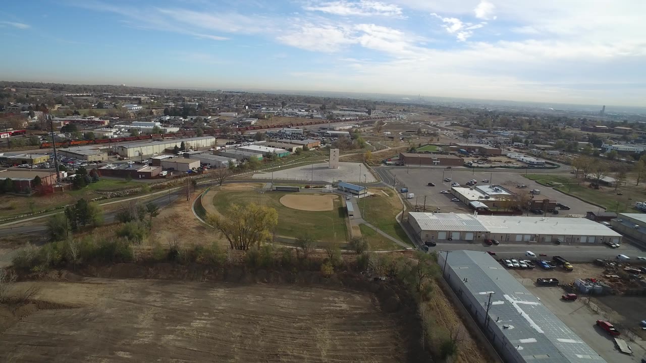 Aerial city view with baseball field, roads, warehouses, and blue sky.
