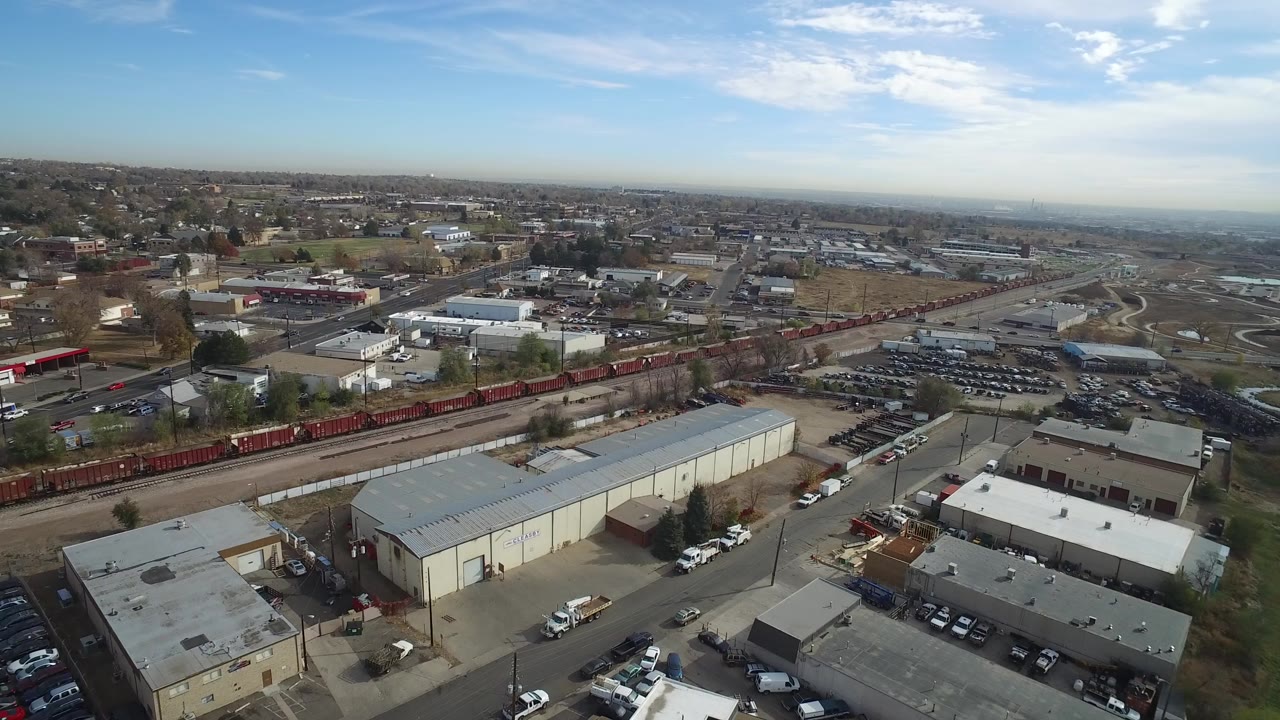 Aerial view over rail cars and warehouse buildings near town streets.