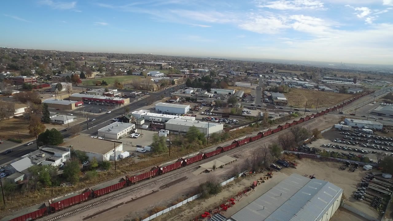 Aerial view of rail cars, roads, warehouses, parking lots, and distant neighborhoods.