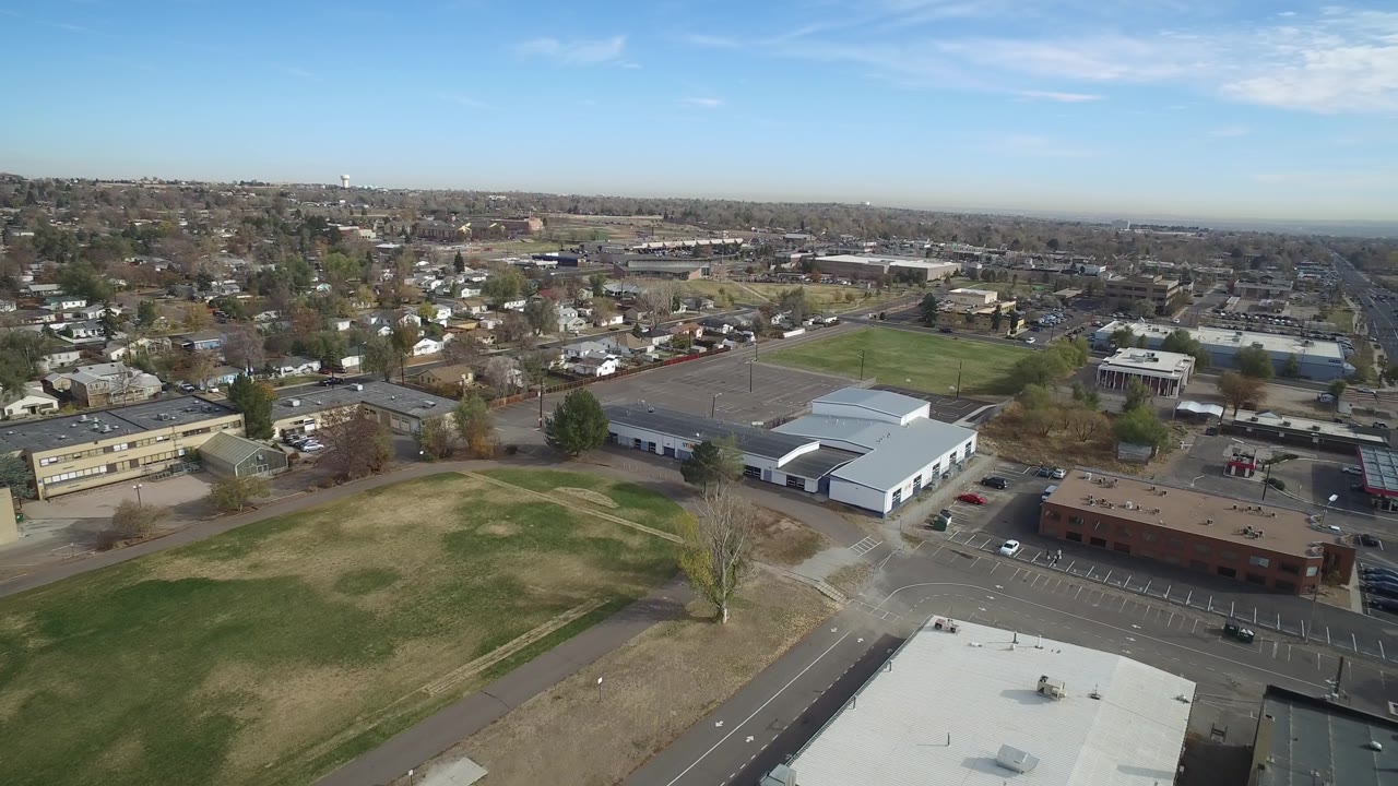 High view of a suburban commercial area beside grass fields and distant neighborhoods.