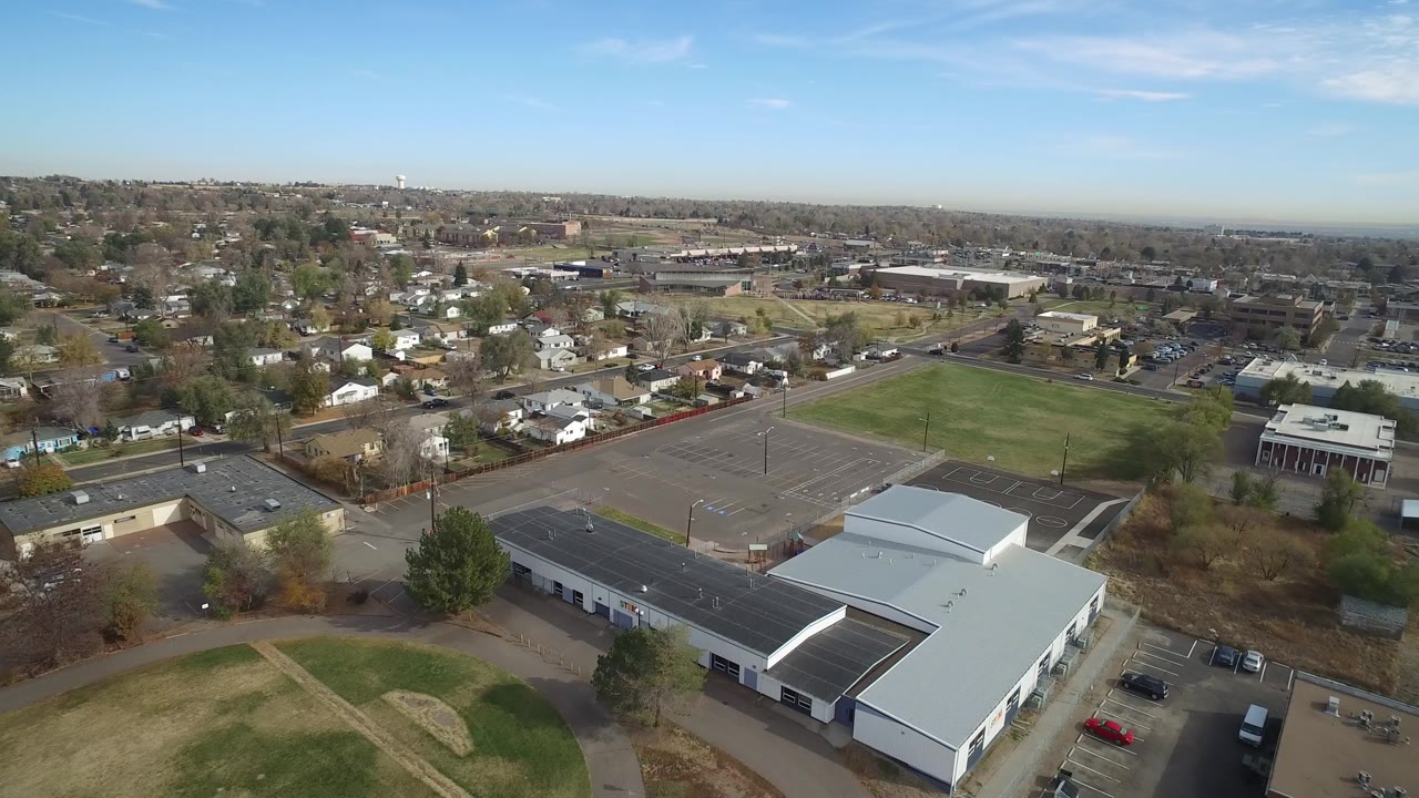 Aerial view of a white-roofed facility beside parking lots and a green field.