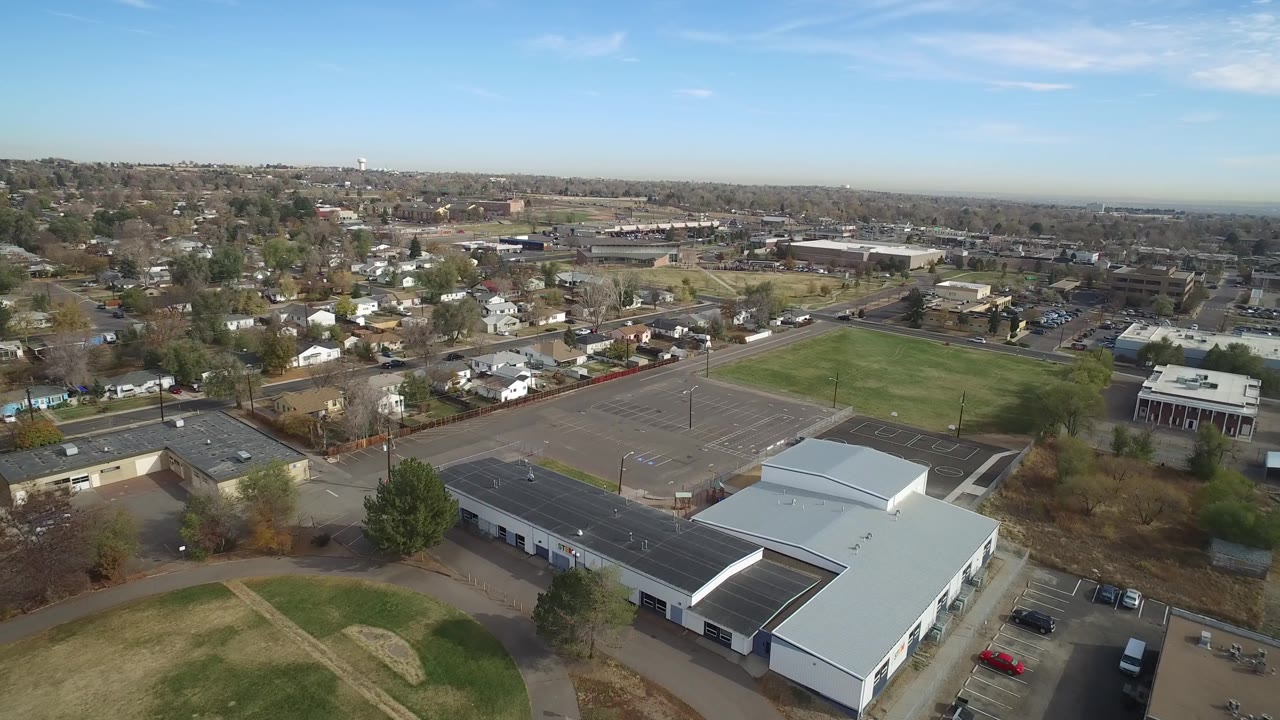 Aerial view in Hidden Lake, Colorado with the white-roofed facility lower in frame, a large paved lot or court area, a rectangular field, neighborhood streets, and no visible people.