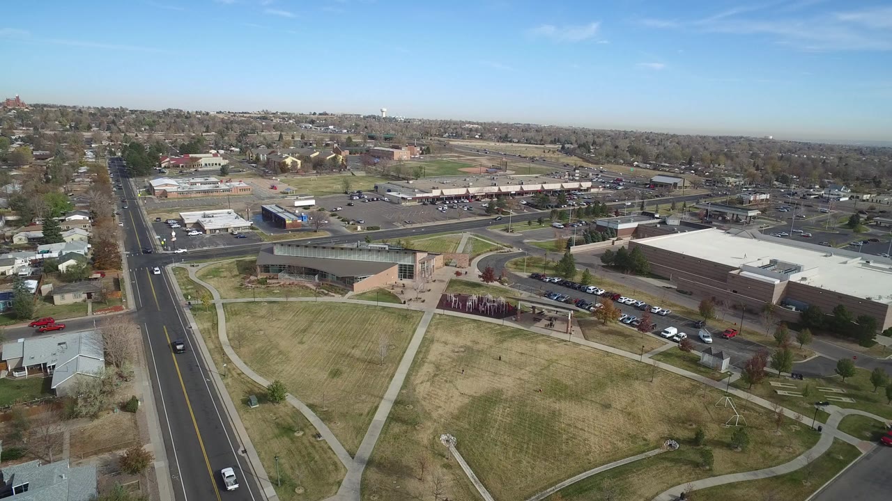 Aerial view over Hidden Lake, Colorado, with a straight road at left, open grass in front, low buildings and parking lots in the middle distance, and no visible people.