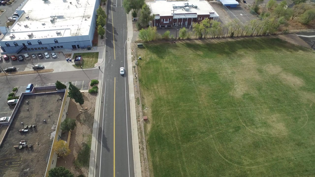 Aerial view of a road beside a grassy field and flat-roofed buildings.