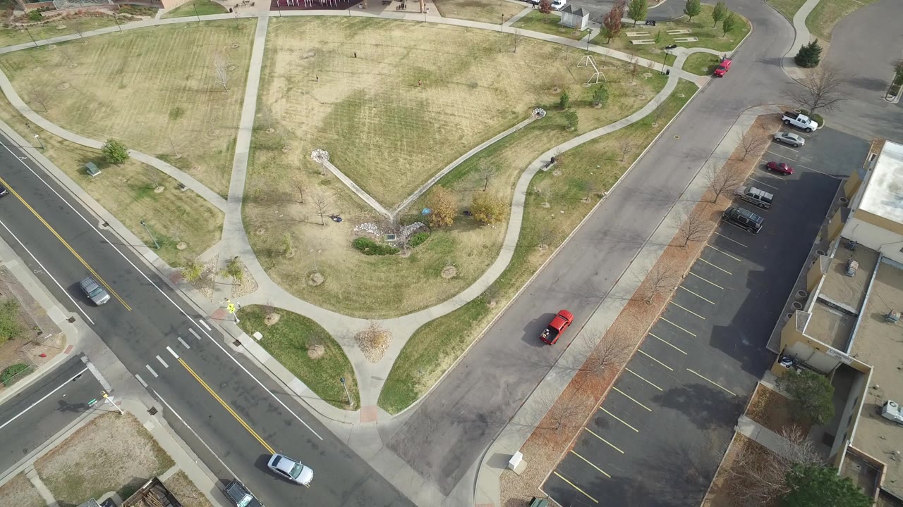 Top-down aerial view of roads, sidewalks, open grass, a parking lot, and cars.
