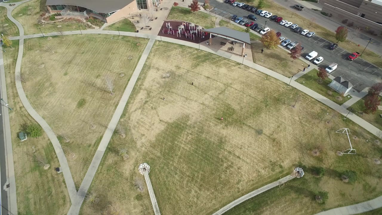 Overhead view of lawns, curved paths, buildings, and parked cars.