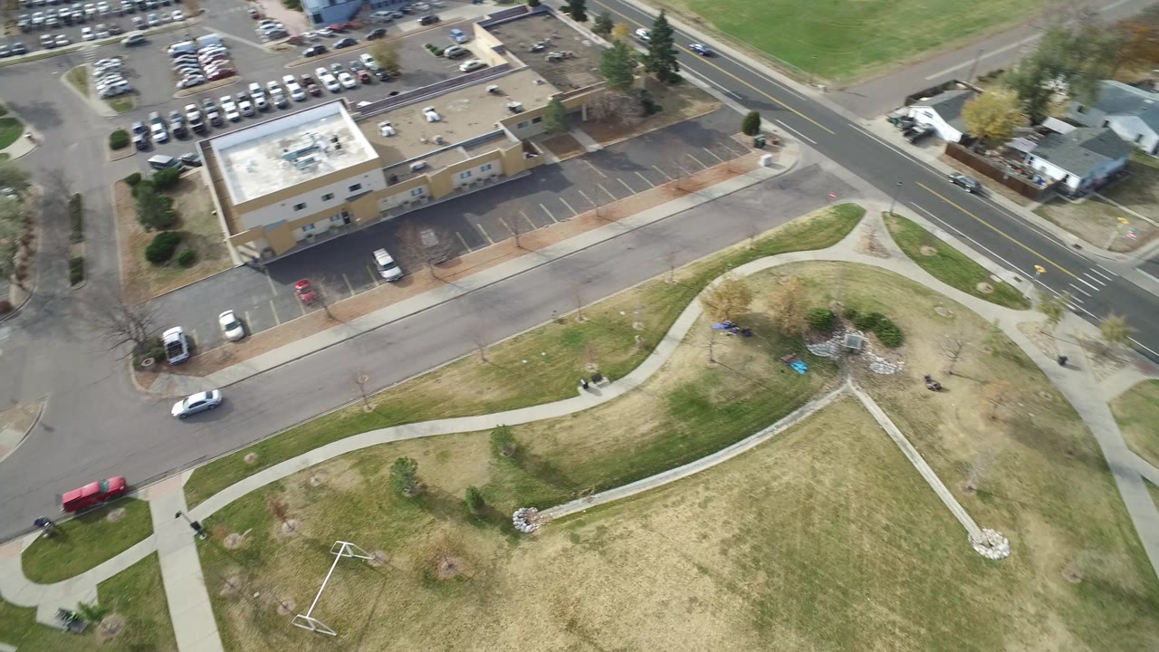 High aerial frame over Hidden Lake, Colorado showing a tan building, parking spaces, surrounding roads, open grass, sidewalks, and no visible people.