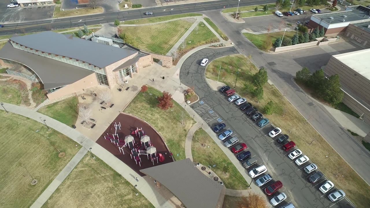 Aerial frame of a building complex with a playground and parked cars beside roads.