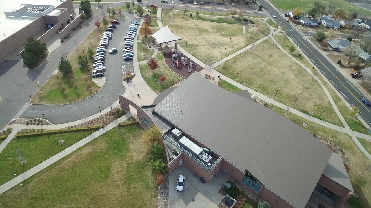 Aerial view of a large roof, curved parking lot, lawns, sidewalks, and a road.