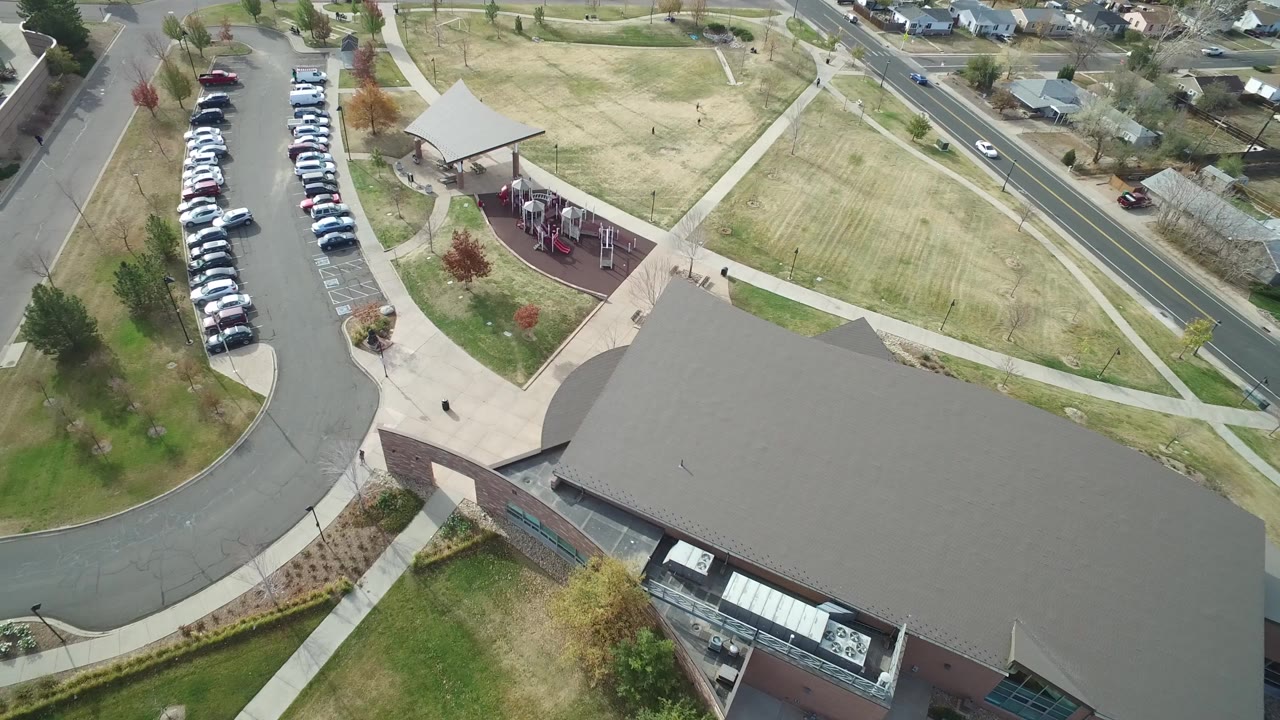 Overhead view of a large building, parking lot, roads, lawns, and nearby houses.