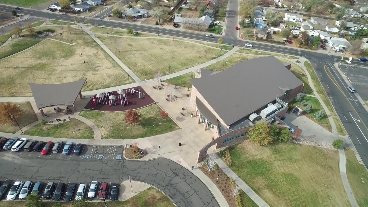 Aerial view of a building, playground, parking lot, roads, and houses.