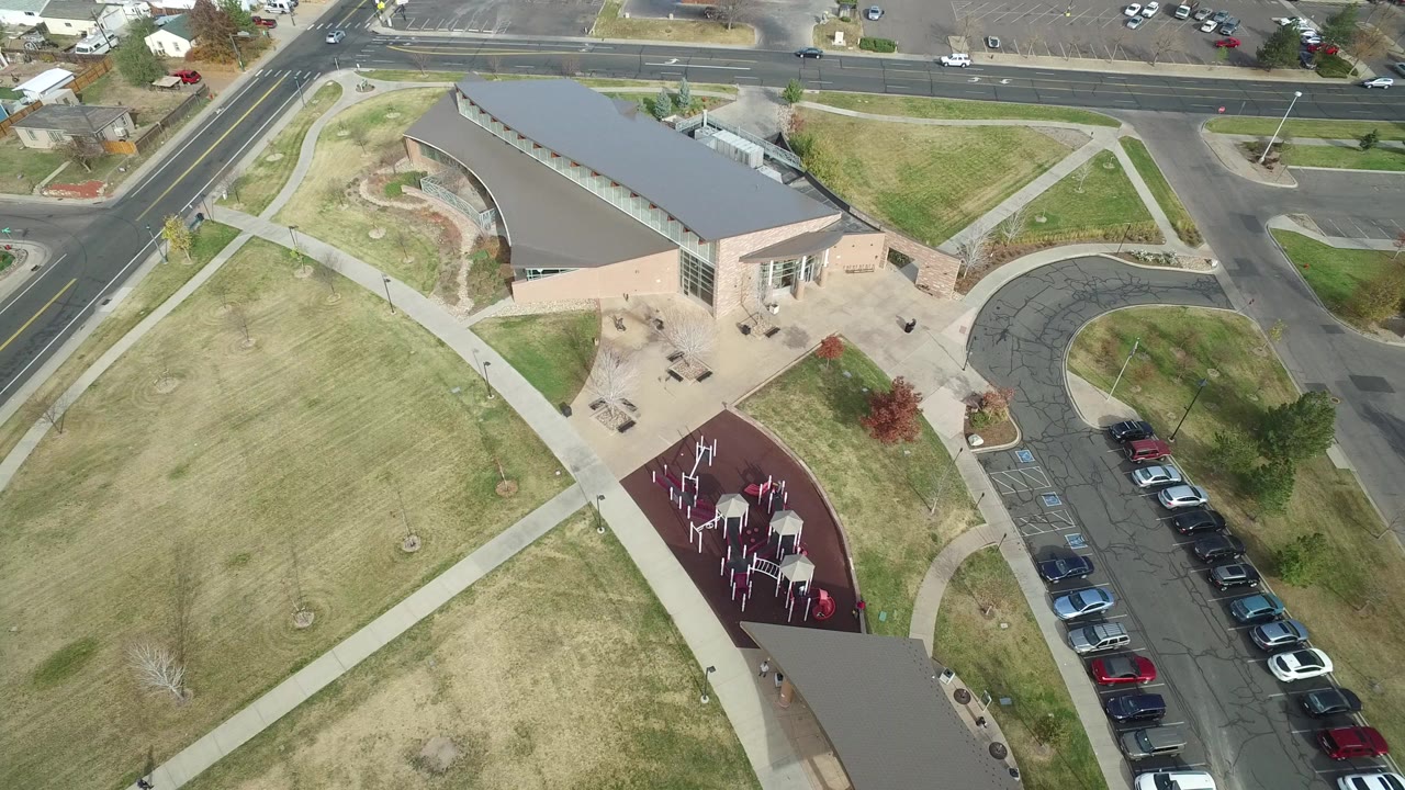 Overhead frame from Hidden Lake, Colorado showing a curved-roof building, grass lawns, a red playground area, parked cars, and public roads, with no visible people.