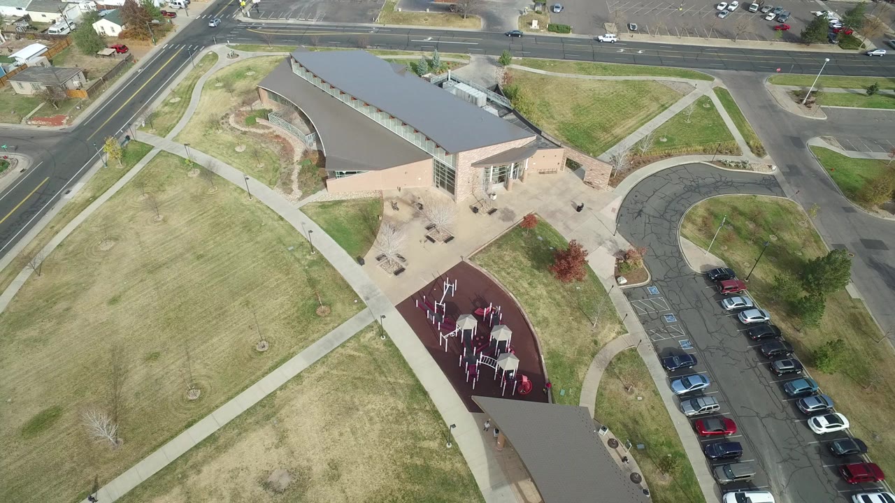 Hidden Lake, Colorado aerial frame with the curved-roof building centered, diagonal sidewalks through lawns, the red playground area below, and parked cars along a lot, with no visible people.