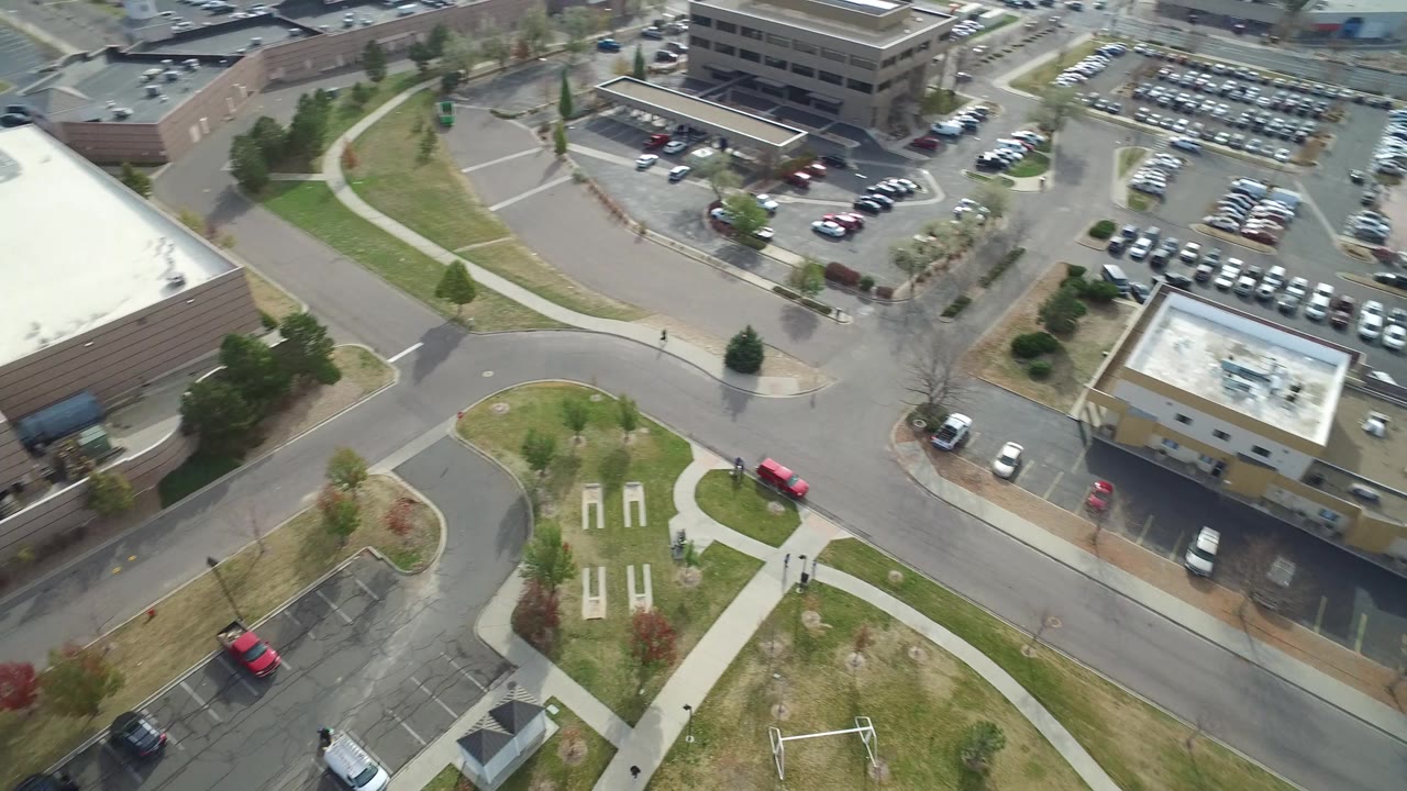 Hidden Lake, Colorado aerial frame with a tan low-rise building near center, surrounding parked cars, curved streets, sidewalks, and open grass, with no visible people.