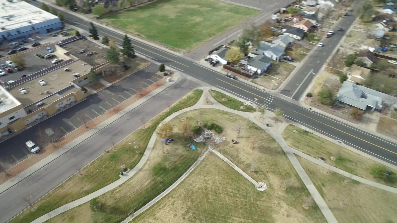 Aerial frame over Hidden Lake, Colorado with the intersection centered higher in the view, curved park paths below, houses along the road, and no visible people.