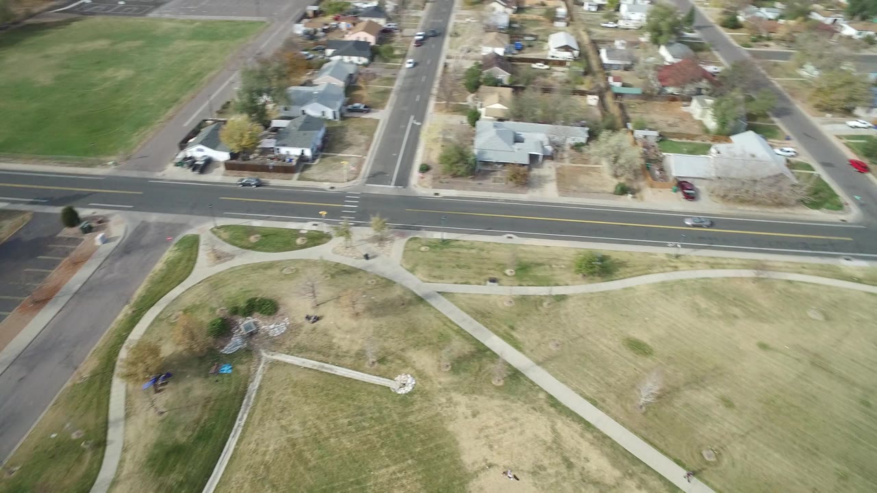 Aerial frame over Hidden Lake, Colorado showing a long road across the upper frame, residential lots behind it, open grass below, and no visible people.