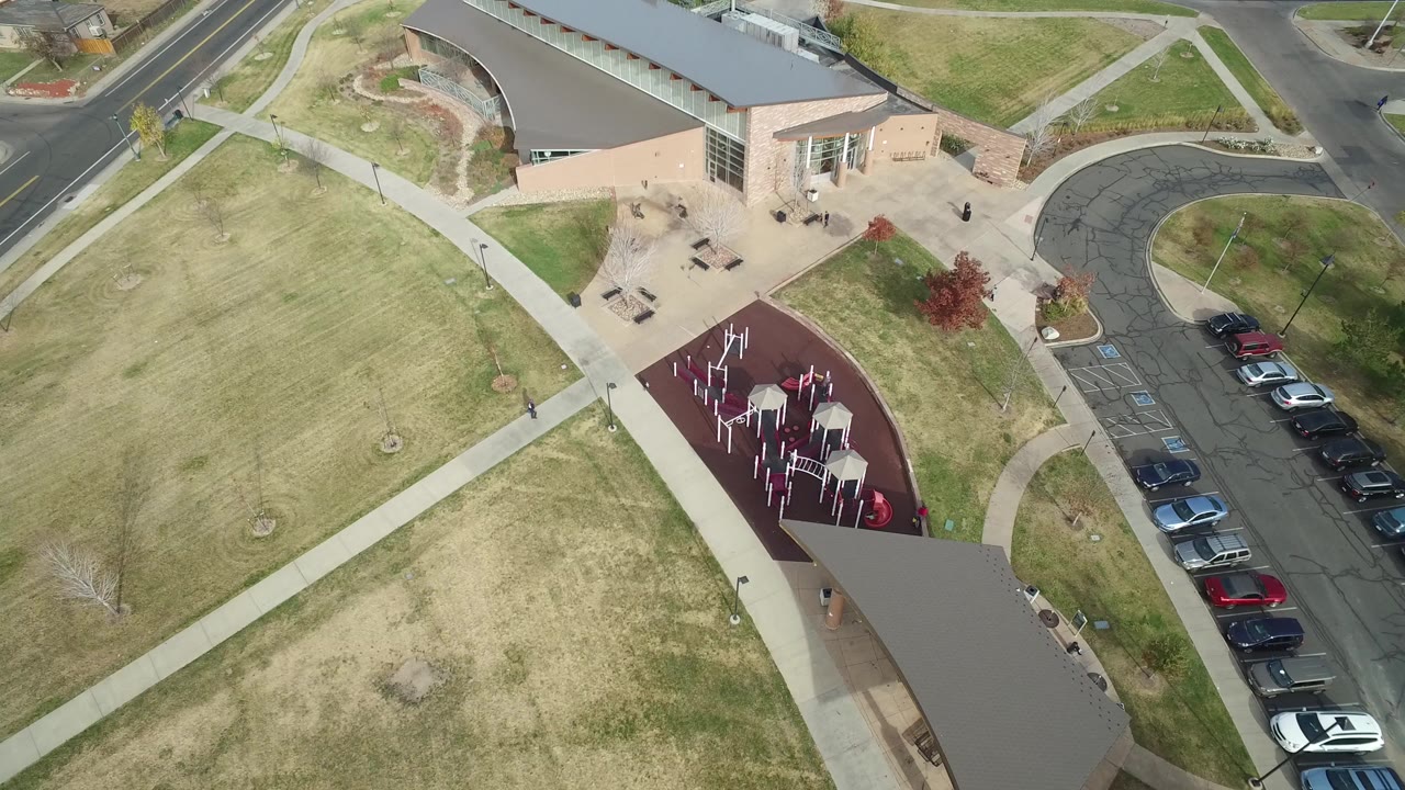 Aerial view of a community building, lawn, walkways, parked cars, and a red play area.