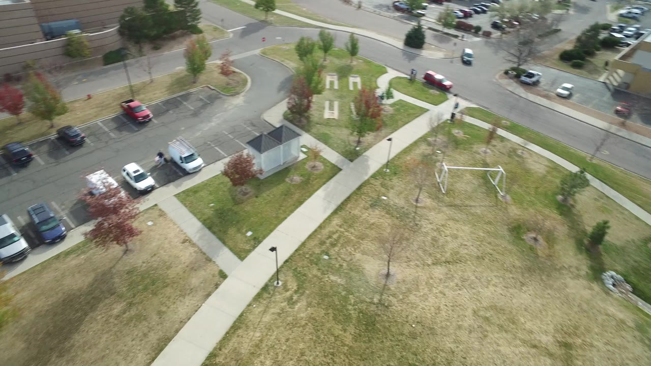 Overhead view in Hidden Lake, Colorado with the sidewalk network centered, a small utility-like structure at lower right, parked cars along the road, and no recognizable people visible.