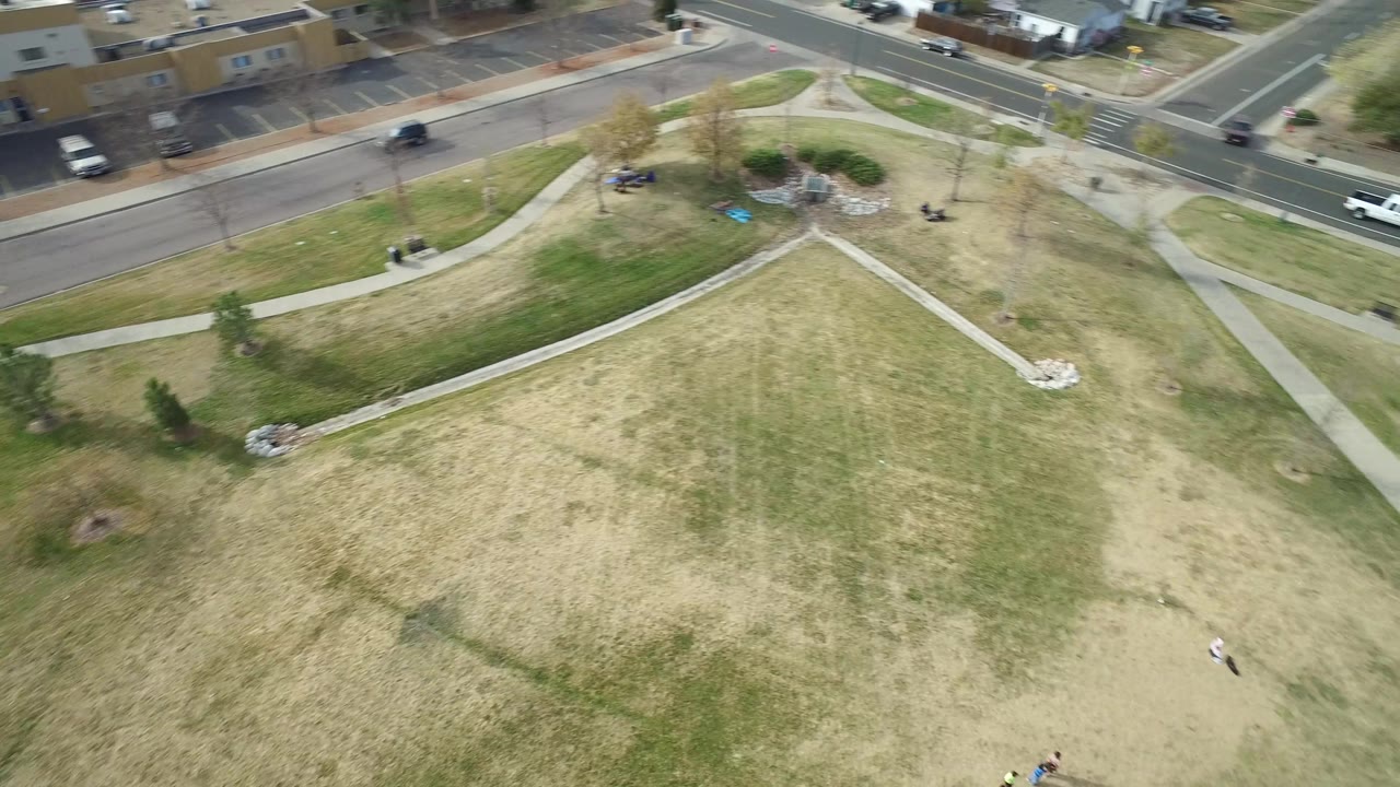 Aerial frame from Hidden Lake, Colorado, with a large grass field, crossing sidewalks, a road at the top, and tiny distant people visible near the lower edge.