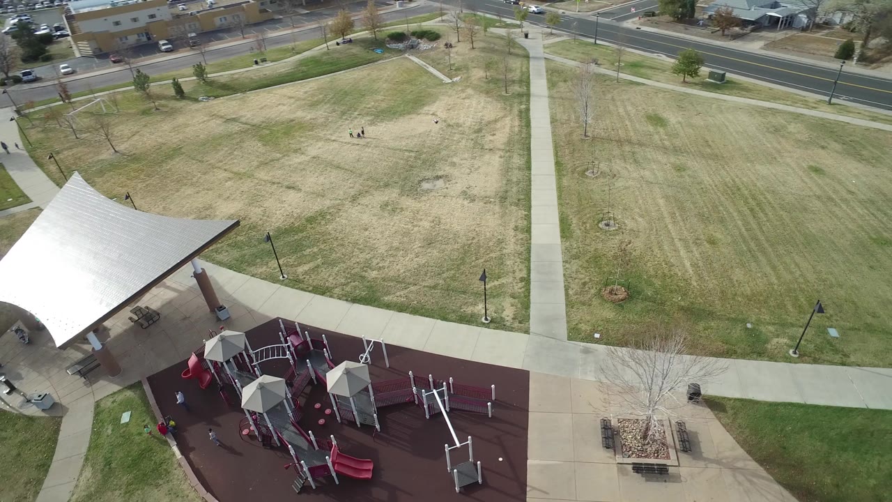 A second Hidden Lake, Colorado aerial frame shows the playground closer to the lower edge, the white tent on the left, intersecting concrete paths, autumn grass, a road, and tiny people visible on the lawn.