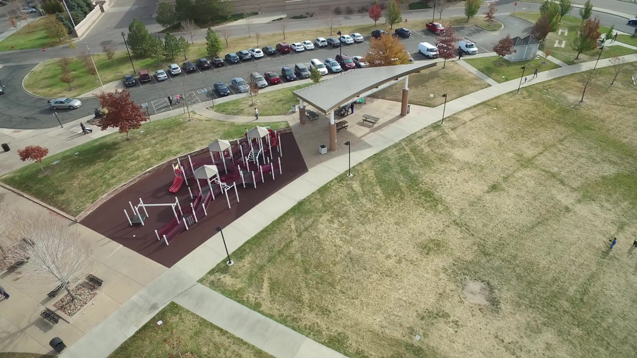 Aerial view of a playground, picnic shelter, lawns, sidewalks, parked cars, and streets.