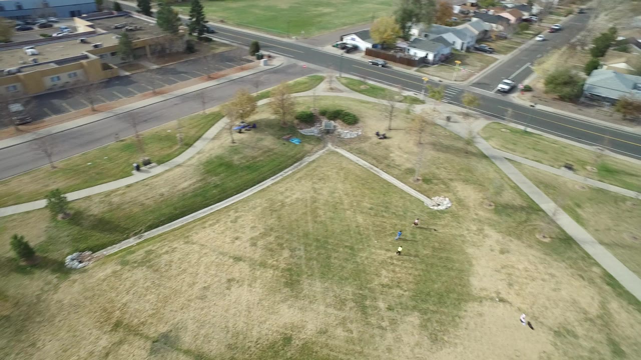 Aerial view of grassy lot with sidewalks, road, homes, and trees.