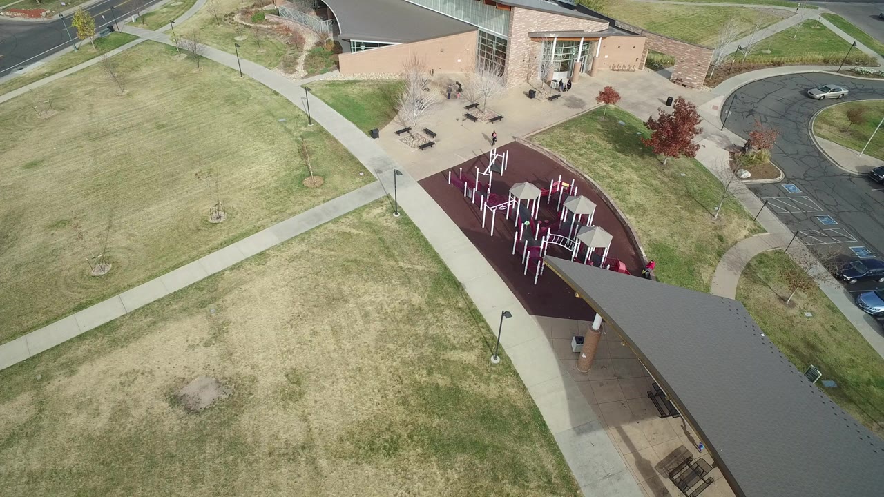 High aerial view in Hidden Lake, Colorado showing open school grounds, intersecting sidewalks, a maroon playground area, and part of the school building with no visible people.