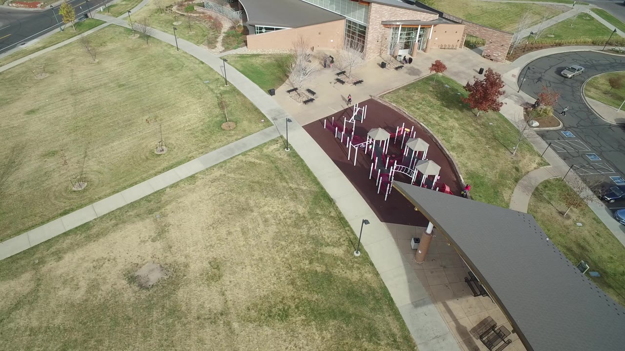 Overhead view of grass, sidewalks, playground, school building, and parking edge.